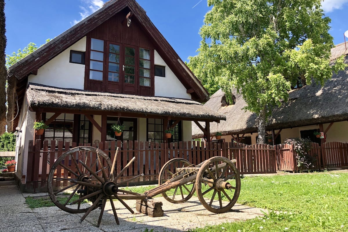 Une maison traditionnelle en bois, avec un toit de chaume, une clôture en bois et une grande charrette en bois au premier plan.