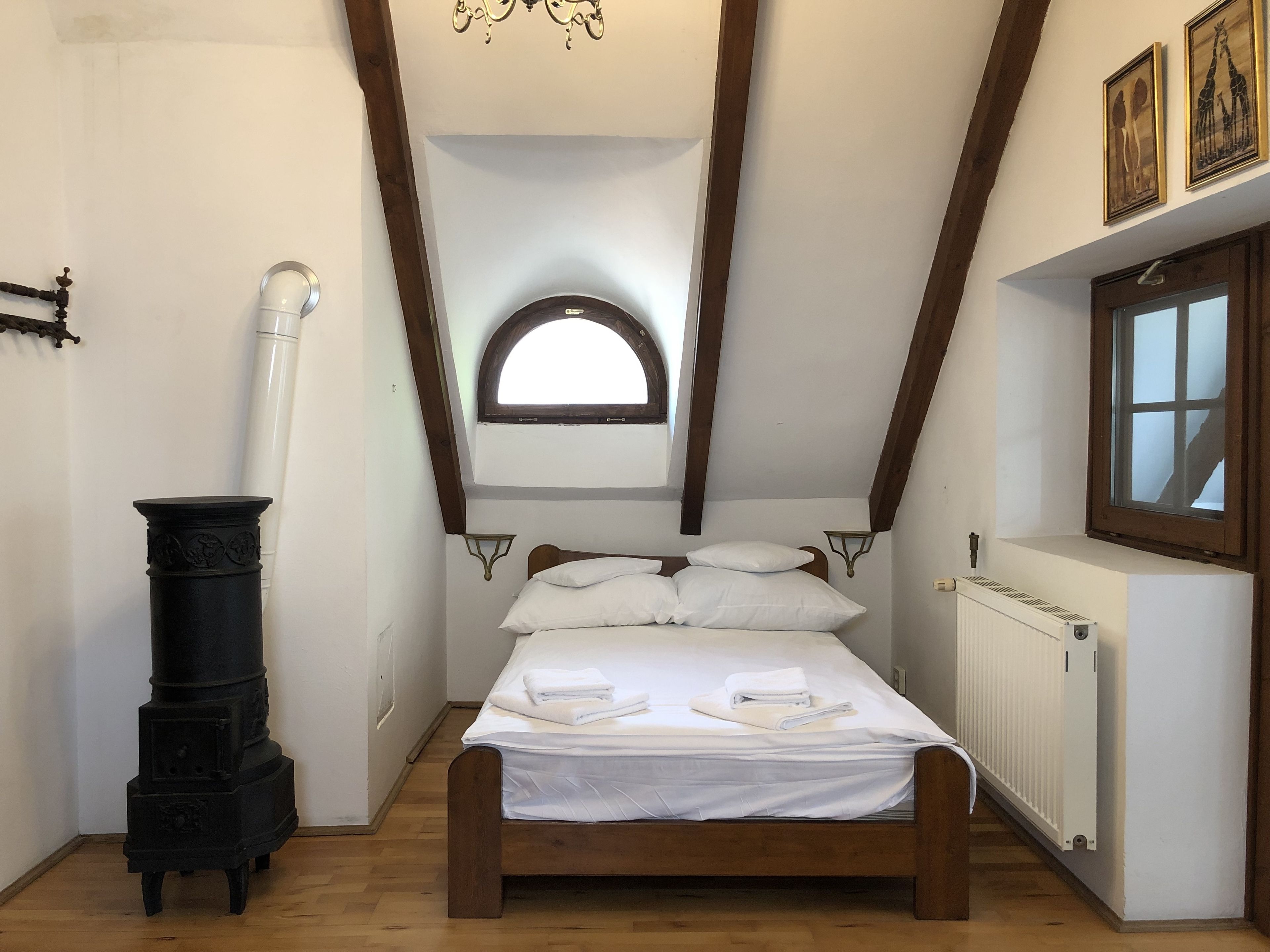 A bedroom with a wooden bed, white linens, a black stove, a window, and a radiator.