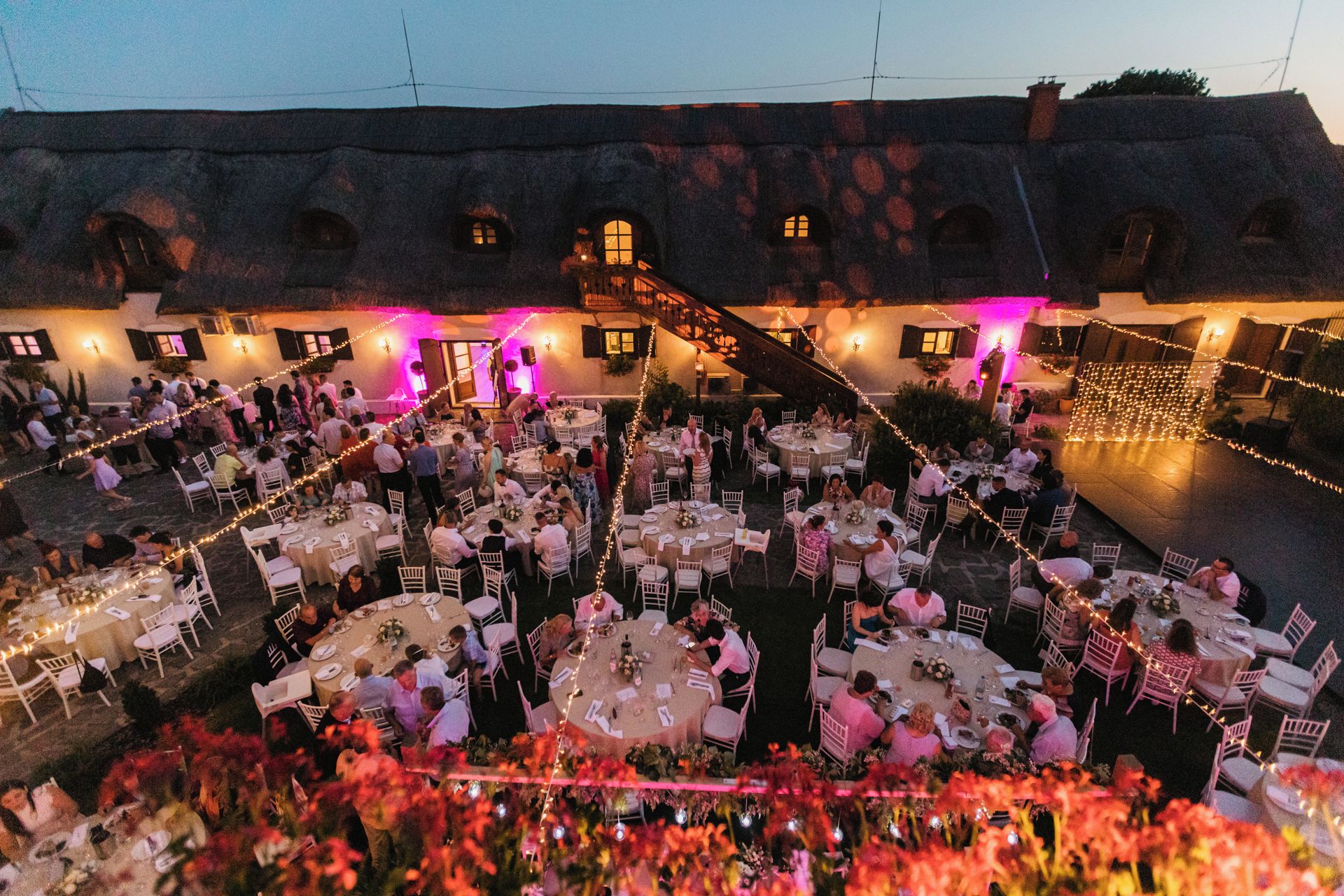 An outdoor wedding reception with round tables and chairs, a staircase, and string lights.