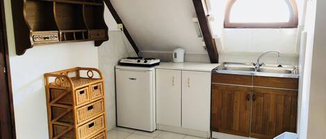 A compact kitchen with white cabinets, a wooden countertop, a sink, and a small refrigerator.