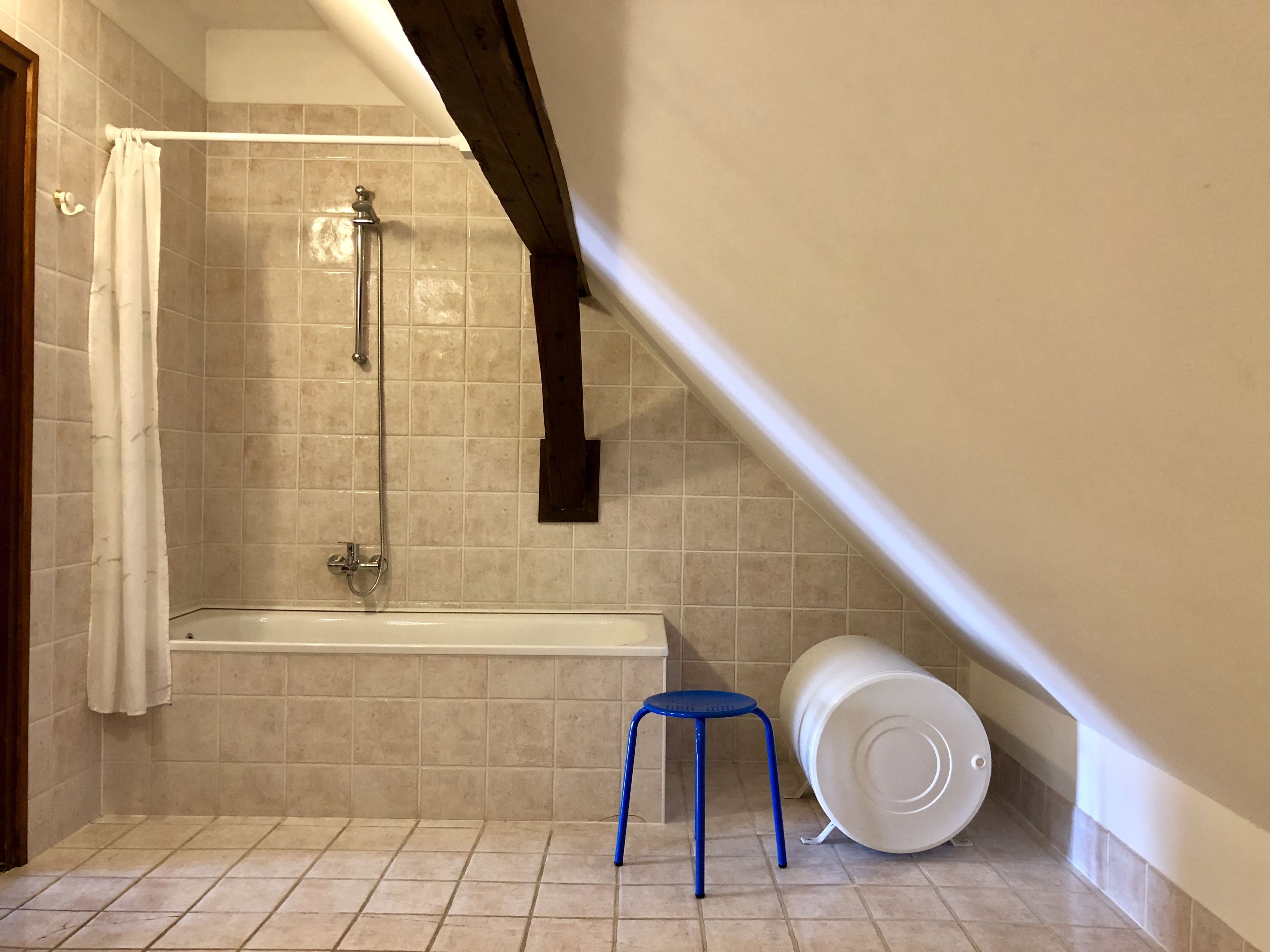 Een kleine badkamer met tegels, een douche, een bad en een blauwe kruk.