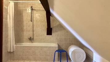 Une petite salle de bain carrelée, équipée d’une douche, d’une baignoire et d’un tabouret bleu.