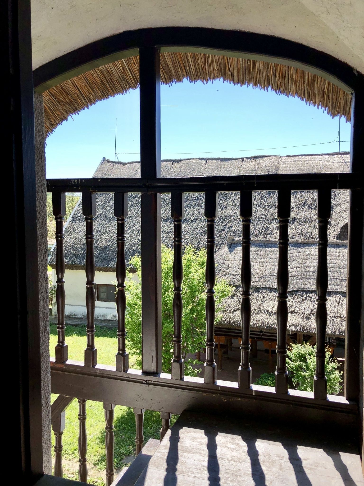 A balcony with a thatched roof, wooden balustrade, and a view of traditional buildings with similar roofs.