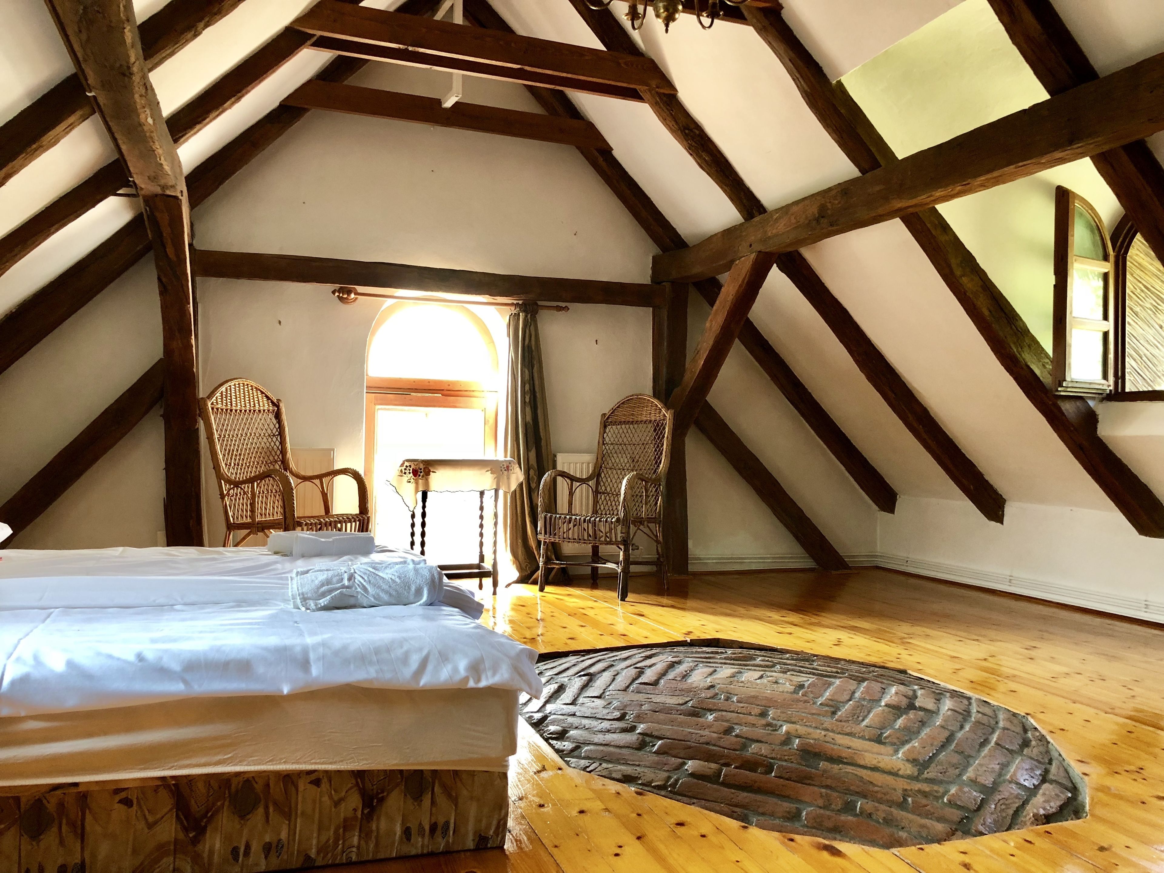 Une chambre avec un plafond en bois, un tapis à motifs de briques et deux fauteuils en osier.