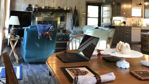 Un ampio soggiorno con soffitto in legno, un divano blu, un tavolo da pranzo con un portatile e un camino.