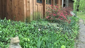 Una baita di legno con un balcone, immersa nel verde e con una statua in pietra.