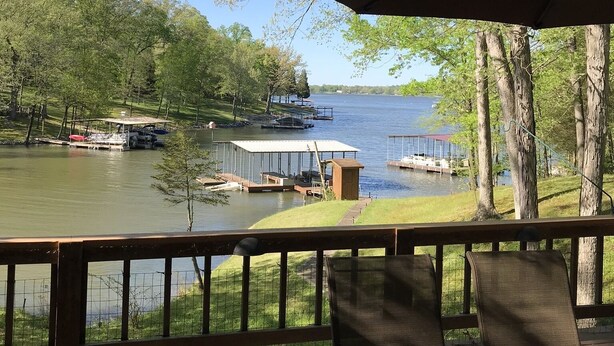 Un terrazzo sul lago con tavolo e sedie, affacciato su un lago con barche e un molo.