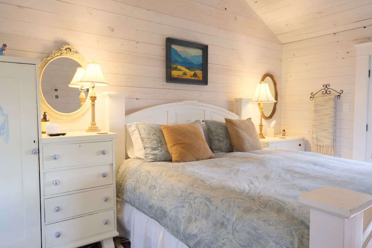 Une chambre à coucher avec un lit, deux tables de chevet avec des lampes, une commode et un miroir.