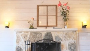 A stone fireplace with a glass door, a rooster figurine, and a vase with flowers on the mantel.