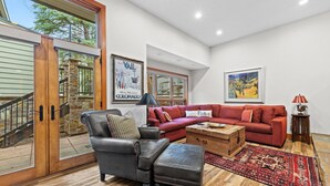 A spacious living room with a leather armchair, red sectional sofa, and a wooden coffee table. A large window offers a view of the outdoors. - Grand Hyatt| Private, tranquil condo with multi level living area and cozy fireplace (Vail)