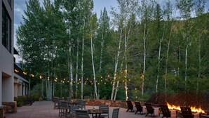 An outdoor patio with tables and chairs, surrounded by trees and a stone wall. - Grand Hyatt| Private, tranquil condo with multi level living area and cozy fireplace (Vail)