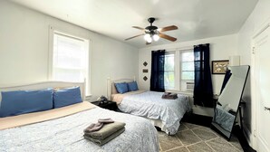 Une chambre avec deux lits, un ventilateur de plafond et une grande fenêtre avec des rideaux.
