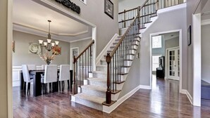 A spacious living room with a hardwood floor, a staircase with a wooden railing, and a dining area with a chandelier.