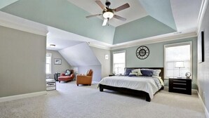 A bedroom with a bed, a chair, a nightstand, a ceiling fan, and a clock on the wall.
