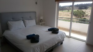 Un dormitorio con una cama grande, una mesita de noche, una lámpara y vistas a un campo de golf a través de una puerta corredera.