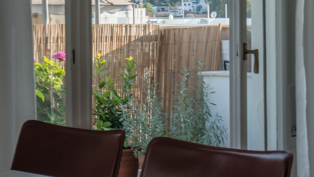 A view from a room with a table and chairs, looking out to a balcony with a wooden fence and some plants. - Ariadne's Penthouse in Central Athens by JJ Hospitality (Athina)