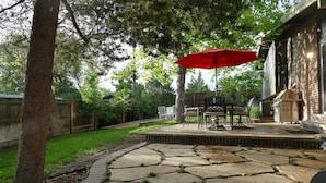 Un patio con suelo de piedra, mobiliario exterior y un paraguas rojo.