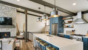 A modern kitchen with a large island, bar stools, a built-in oven, and a stone fireplace. - Schweitzer Luxury Ski in/out Townhome | Hot Tub (Sandpoint)