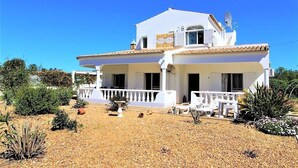 A two-story white building with a tiled roof, a balcony, and a garden area with plants and a gravel path. - Villa in Algarve with complete privacy (moncarapacho,)