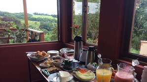 A breakfast buffet with various food items and beverages, set against a backdrop of a scenic view through large windows.