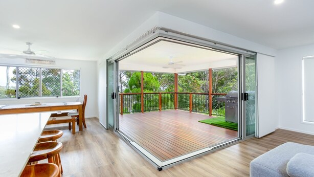 A modern kitchen with a dining area, a sliding glass door leading to a deck with a barbecue grill. - 25 Cooloola Drive - Rainbow Beach. Stunning, Modern, Open Plan Beach House. Wifi. (RAINBOW BEACH)