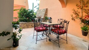 Une terrasse extérieure avec une table et des chaises, entourée de plantes en pot et d’un mur de pierre.