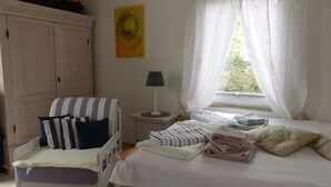 A bedroom with a bed, a chair, a nightstand, a lamp, a wardrobe, and a window with curtains.