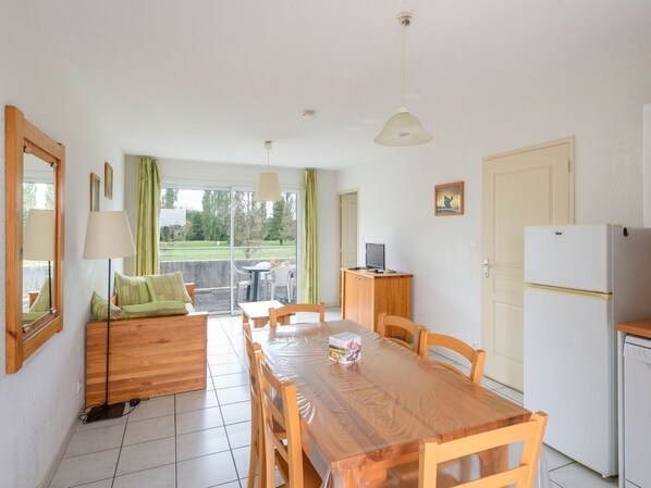 A compact kitchen with a dining table, chairs, a refrigerator, and a small TV on a wooden cabinet. - Appart sympa proche du Golf, accès Piscine (Rivières)