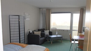 A hotel room with a bed, a sofa, a small table, a chair, and a window with curtains. - This 30 m&sup2; vacation apartment (west-facing) is located on the 6th floor of the Kiel building. A double bed and two sleeper chairs can accommodate up to 4 people. . <br><br>The built-in kitchen is fully equipped for self-catering. The cozy one. (Schönberg OT Holm)