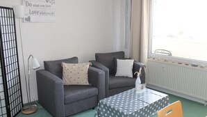 A room with two grey sofas, a small table with a polka dot tablecloth, a white radiator with decorative stones, and a sign on the wall. - This 30 m&sup2; vacation apartment (west-facing) is located on the 6th floor of the Kiel building. A double bed and two sleeper chairs can accommodate up to 4 people. . <br><br>The built-in kitchen is fully equipped for self-catering. The cozy one. (Schönberg OT Holm)