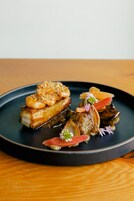Un plato de comida con diversos mariscos, incluyendo camarones y vieiras, sobre un plato oscuro.