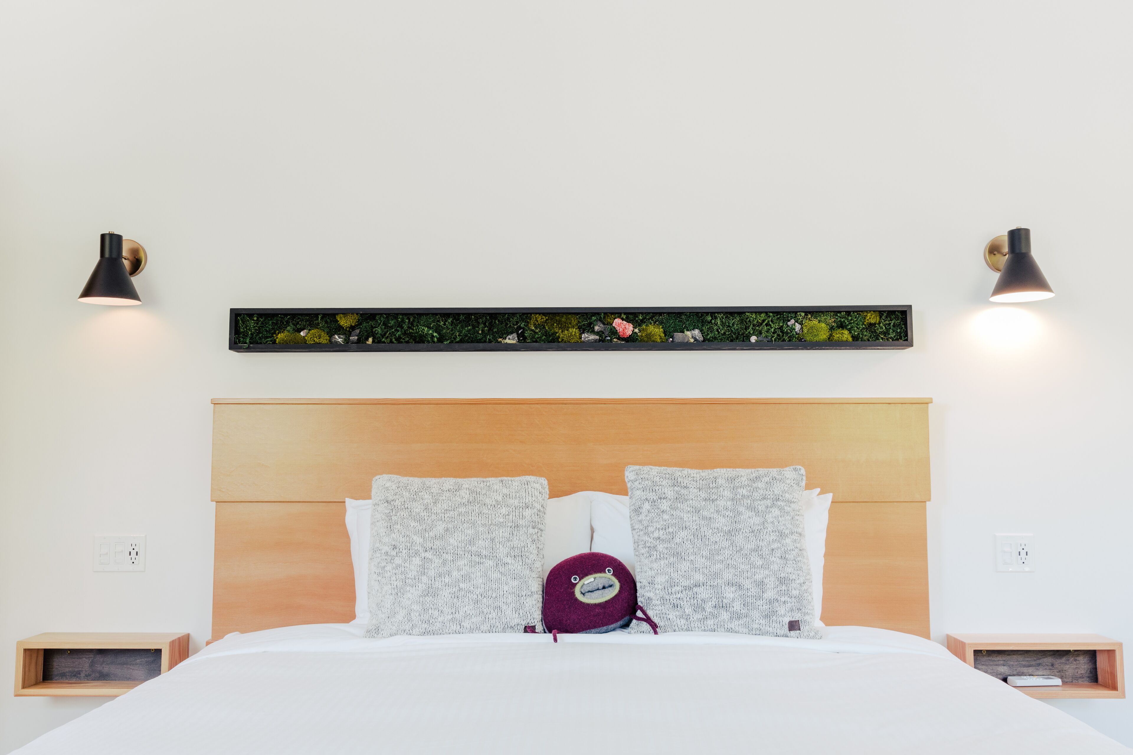 A neatly made bed with a wooden headboard, two bedside tables, and a wall-mounted shelf with a decorative arrangement.