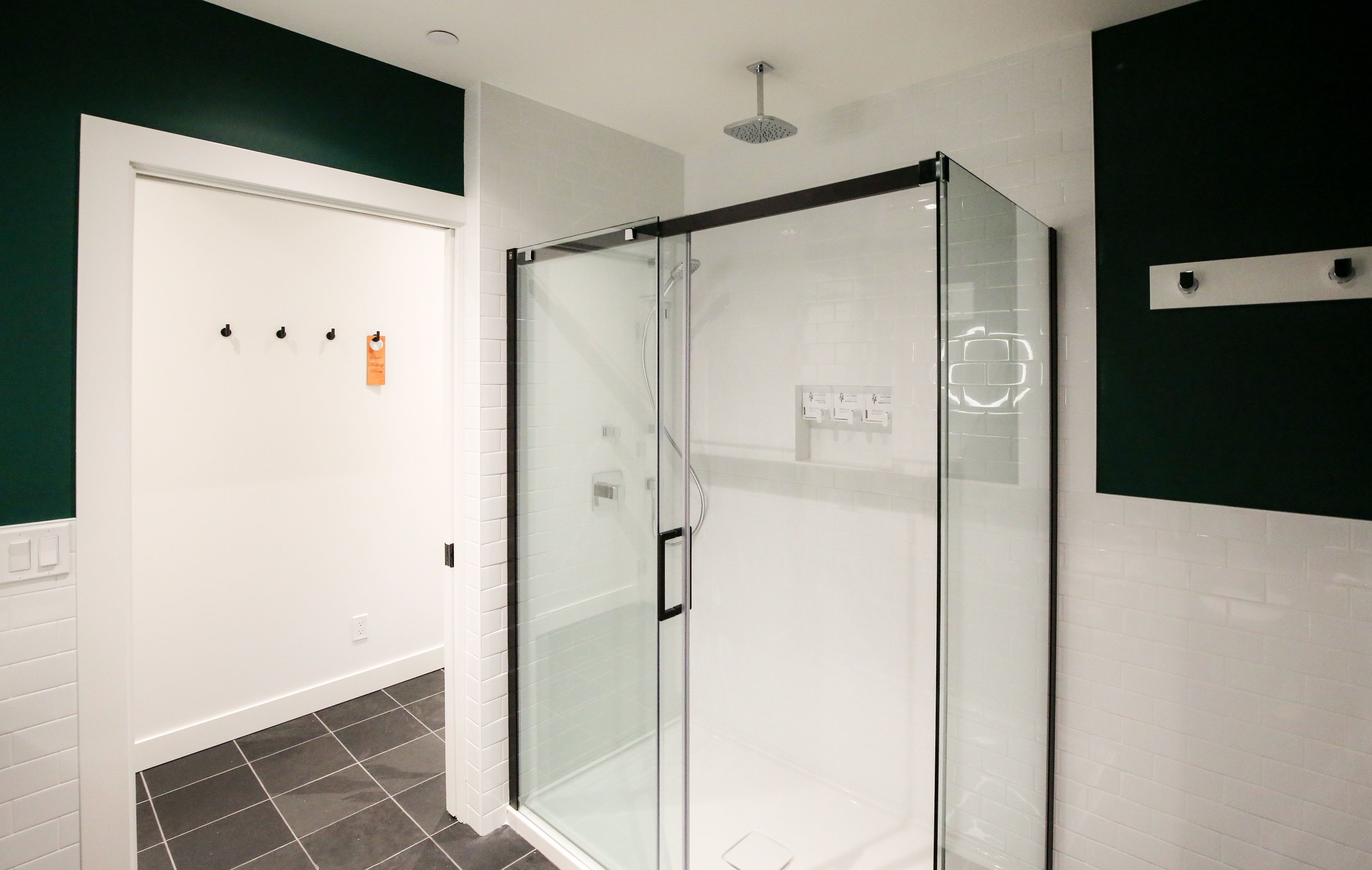 A modern bathroom with a glass-enclosed shower, white tiled walls, and a green accent wall.