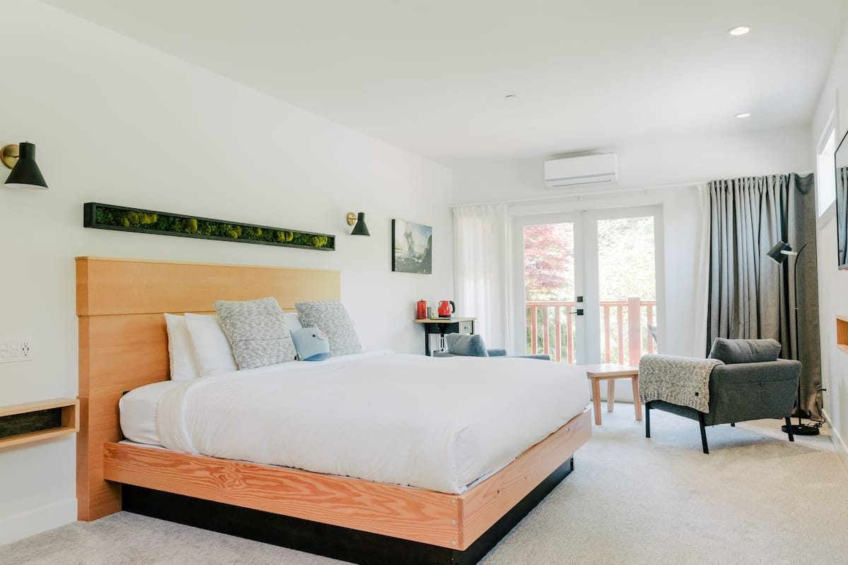 A modern bedroom with a wooden bed, a small table, a chair, and a balcony with curtains.