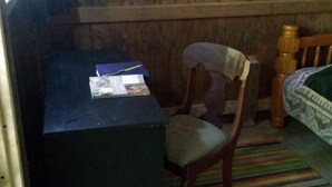 A small, dimly lit room with a wooden desk, a chair, and a bed with a patterned bedspread. - Coyote's Den Rustic Cabin  for Adventurous Camper (Freeville)