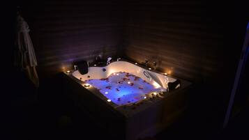 A dimly lit room with a large bathtub filled with water and rose petals, surrounded by candles.