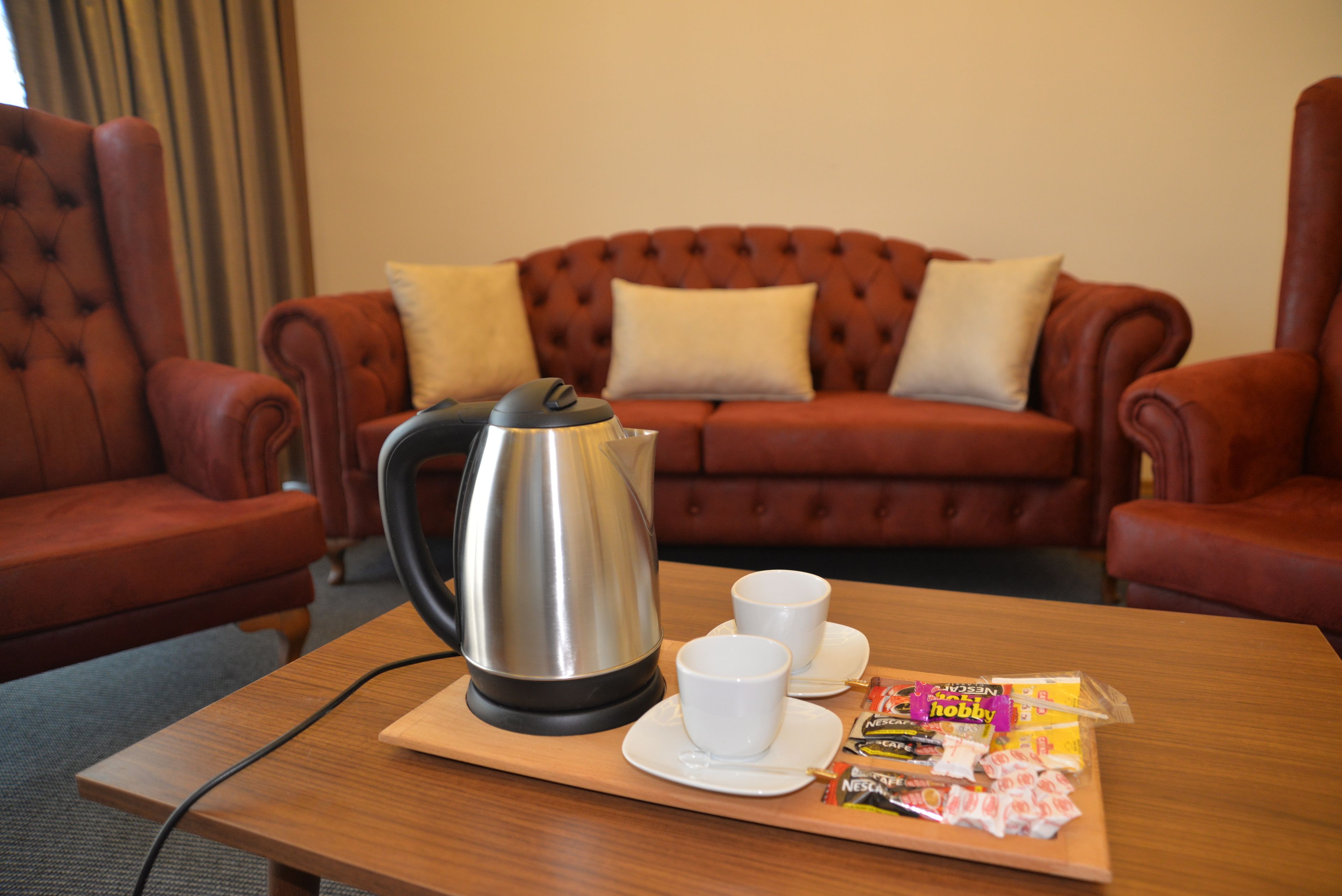 A cozy living room with a red leather sofa, a wooden coffee table with a kettle, cups, and a tray of snacks.