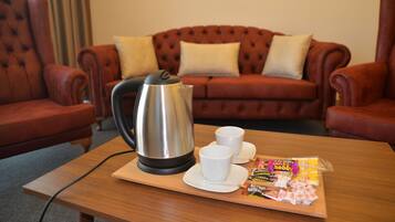 A cozy living room with a red leather sofa, a wooden coffee table with a kettle, cups, and a tray of snacks.