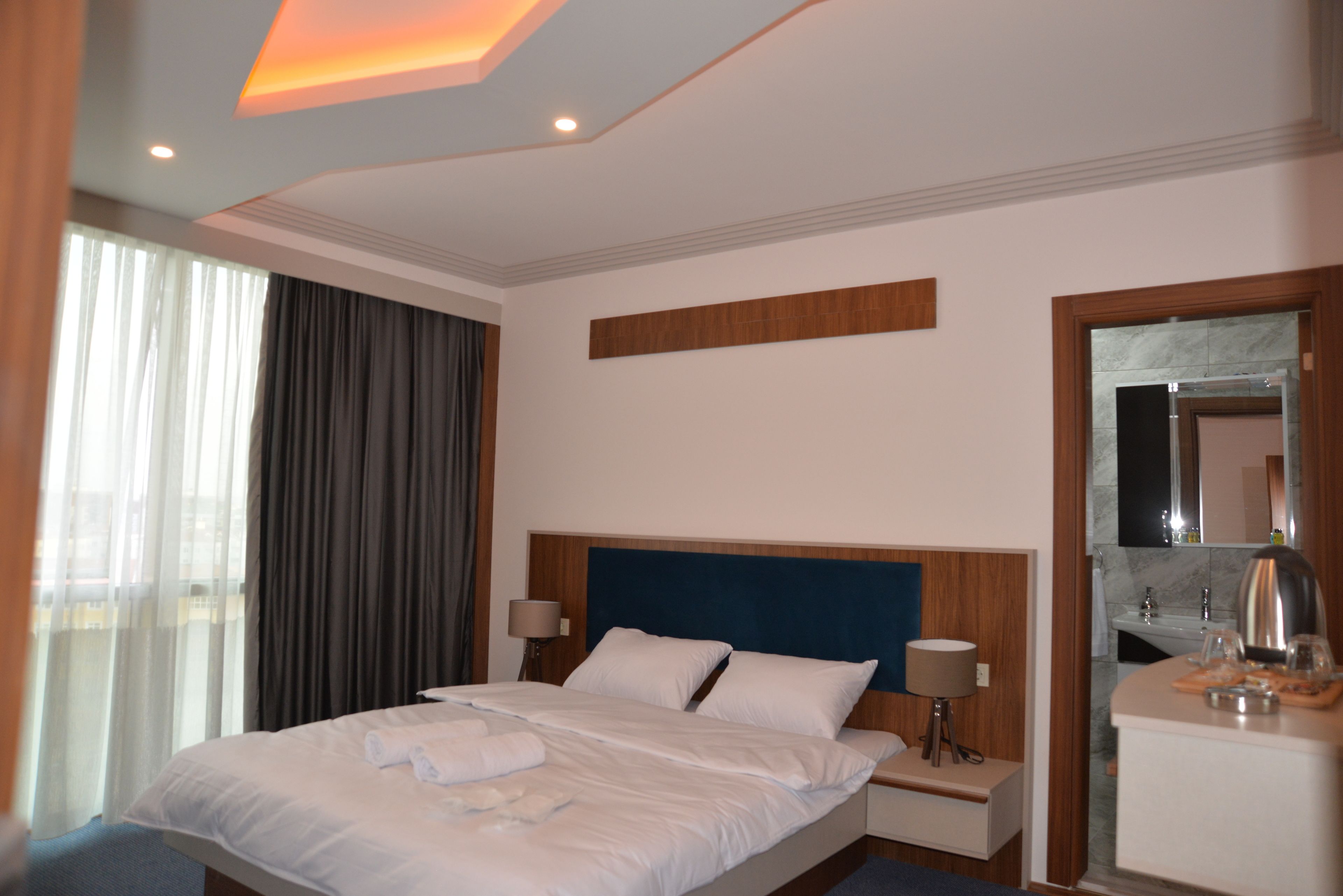 Una habitación de hotel con una cama grande, una mesita de noche, un espejo y una ventana con cortinas.