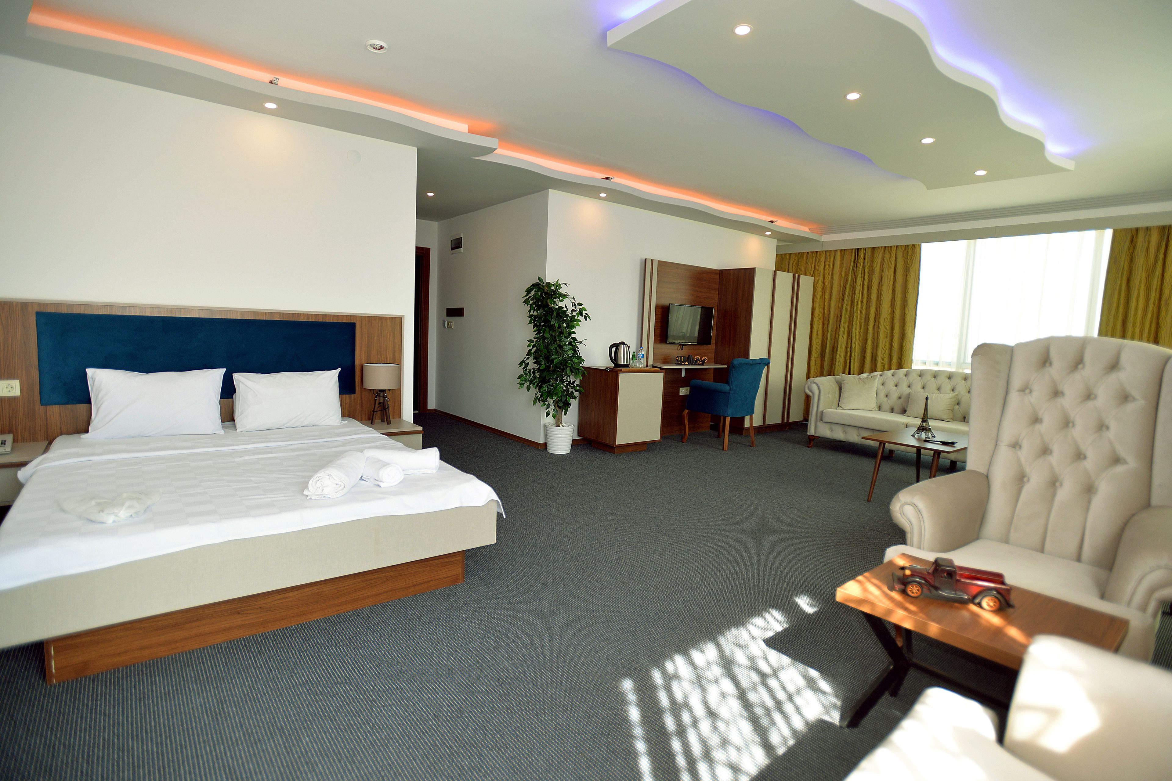 A hotel room with a large bed, a desk, a chair, a sofa, and a TV.
