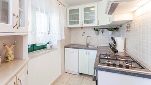 A compact kitchen with white cabinets, a gas stove, a sink, and a window with sheer curtains. - Holiday house Layla in Tucepi, sea view (Tucepi)