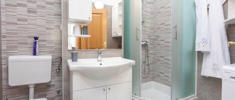 Une salle de bain moderne avec un lavabo, des toilettes et une douche, le tout de couleur blanche.