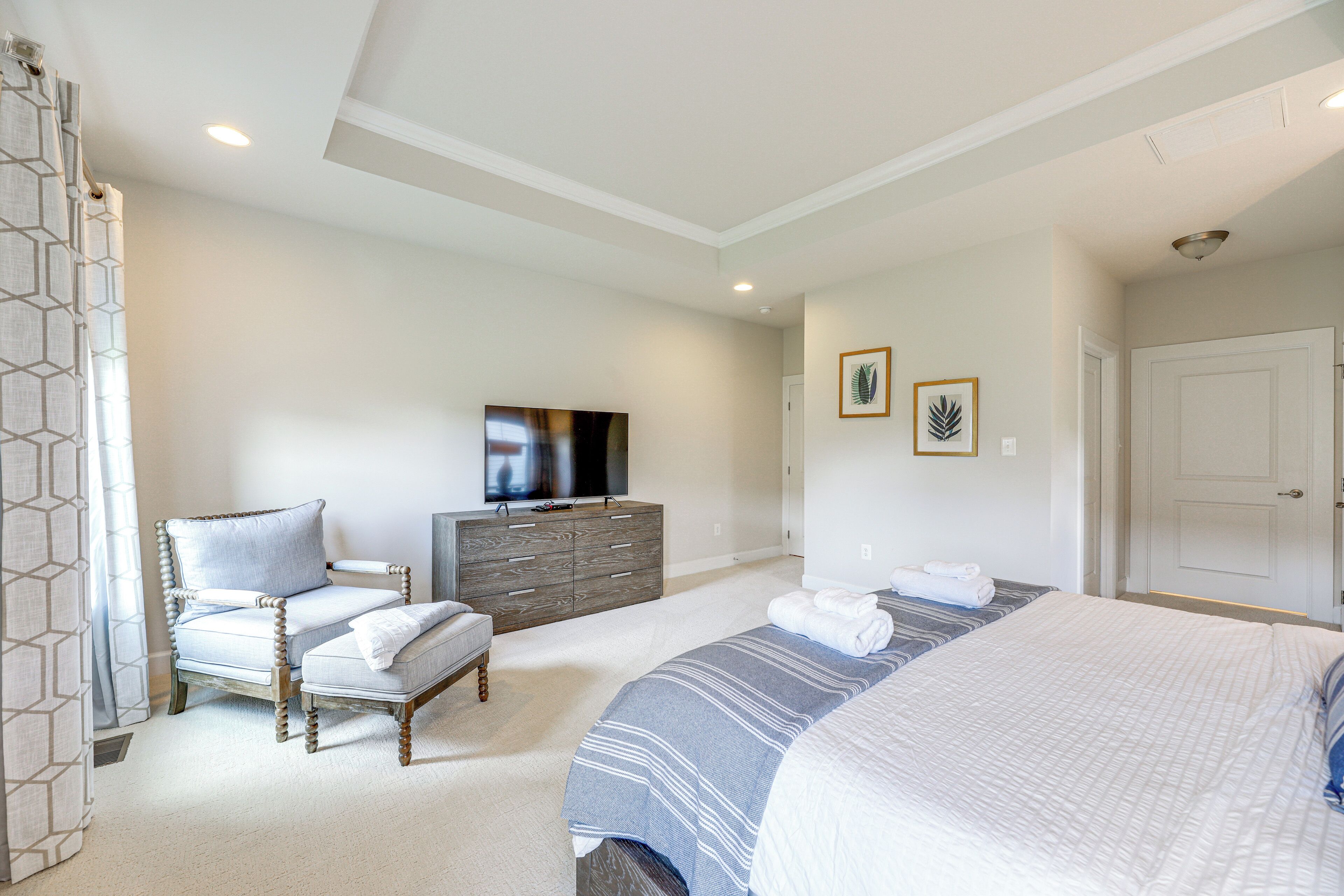 Une chambre à coucher avec un lit, une chaise, une commode, un téléviseur et une porte.