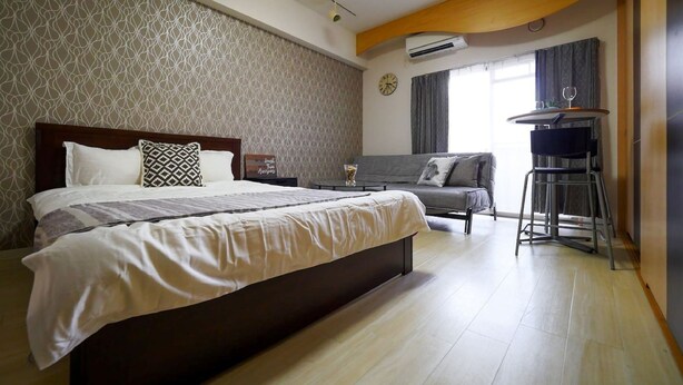 A hotel room with a large bed, a sofa, a small table, and a window with curtains. - City central studio Apartments (Osaka)