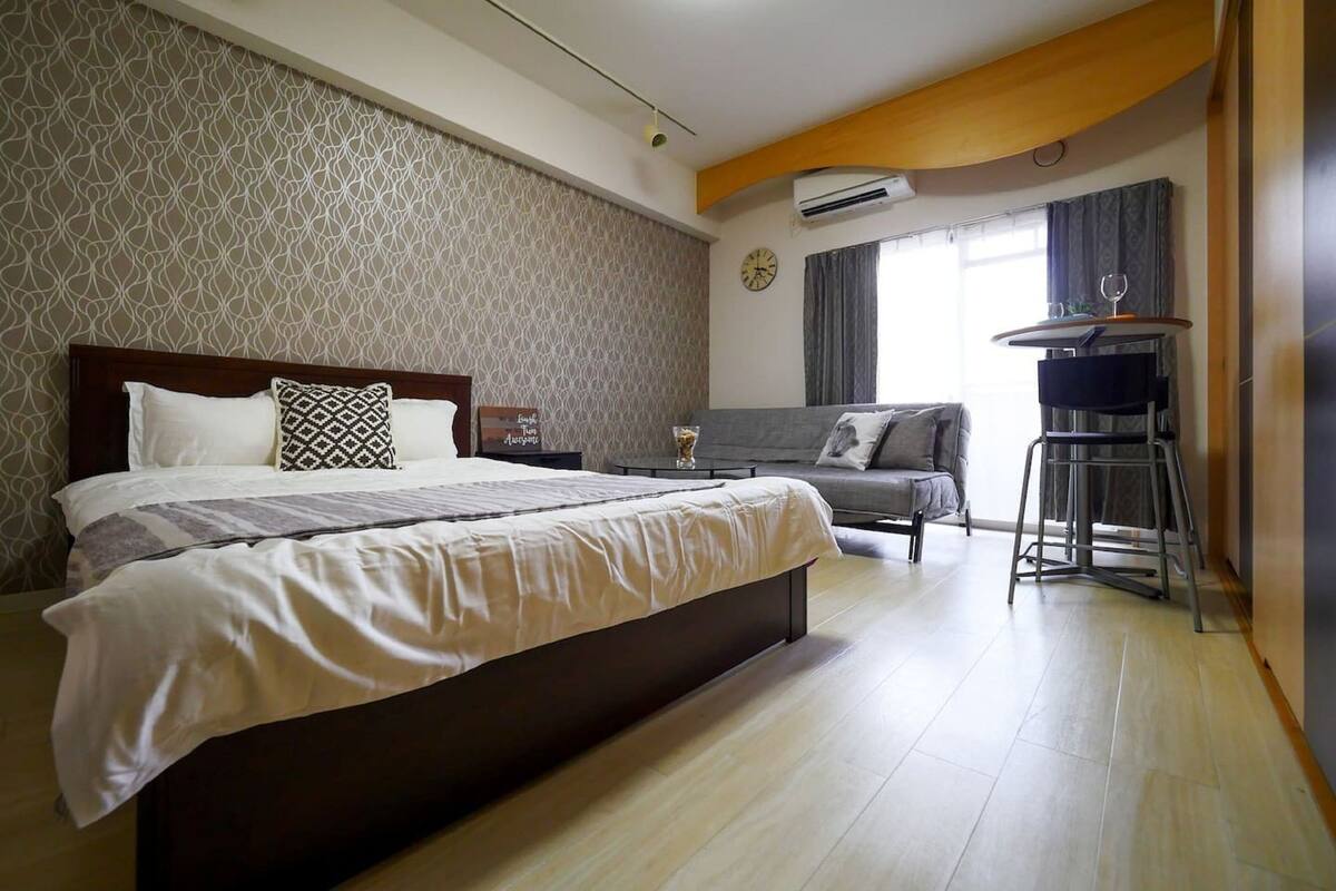 Una habitació d'hotel amb un llit gran, un sofà, una taula petita i una finestra amb cortines.