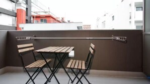 A balcony with a table and two chairs, a metal railing, and a view of buildings in the background. - City central studio Apartments (Osaka)