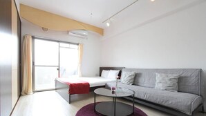 A modern living room with a sofa, a round coffee table, and a bed with a red blanket. - City central studio Apartments (Osaka)
