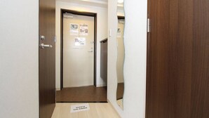 A narrow hallway with a wooden door at the end, a small mat on the floor, and a mirror on the wall. - City central studio Apartments (Osaka)