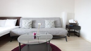 A modern room with a grey sofa, a glass coffee table, a white bed, and a small black side table with a tissue box. - City central studio Apartments (Osaka)
