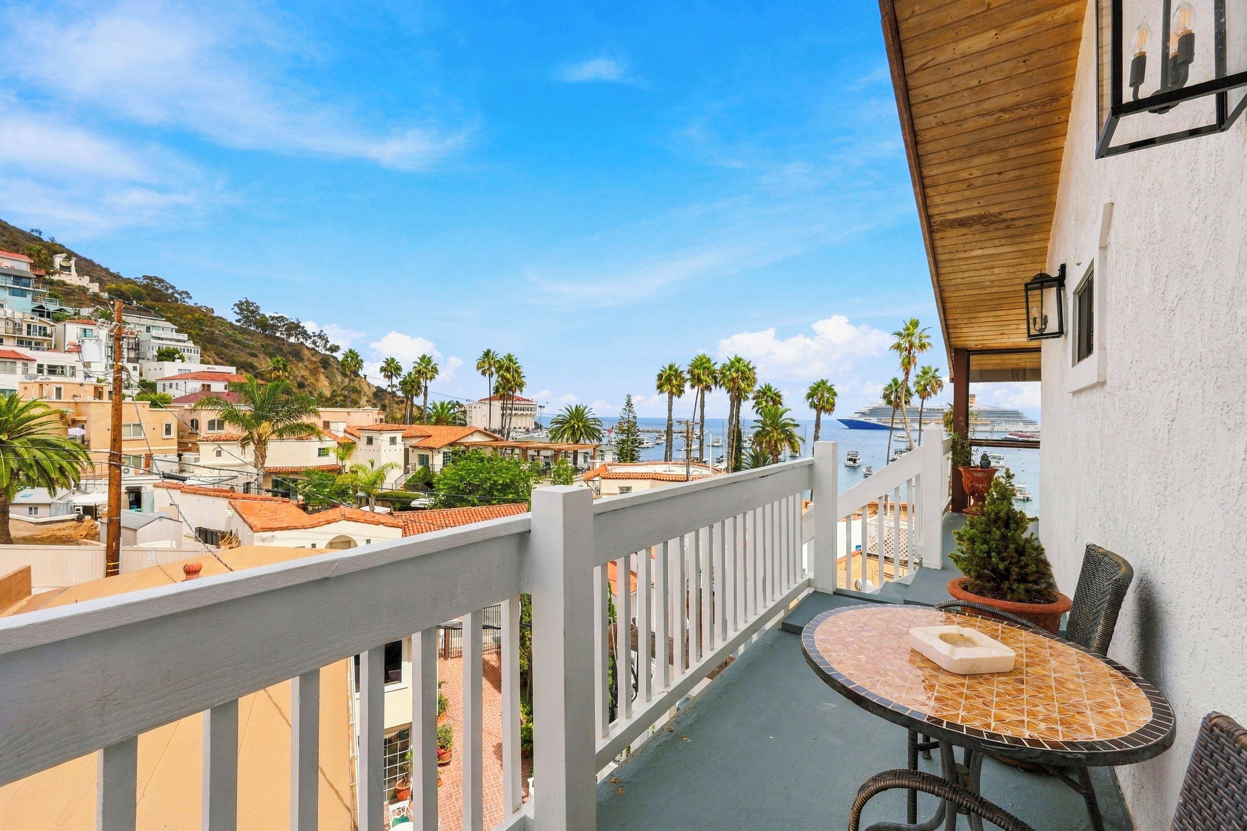 A balcony with a view of a coastal town, a table with chairs, and a potted plant.